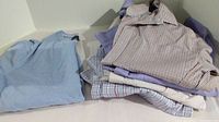Four Tommy Hilfiger button-down shirts stacked with a light blue Banana Republic sweater beside them.