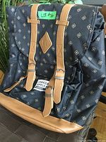 Large black and brown backpack with diamond pattern and leather straps, labeled Canada Supply Goods