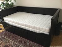 Side-on view of assembled black IKEA daybed with mattress