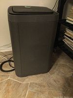 Front view of the large rectangular dark gray plastic garbage can with lid closed and textured floor tiles.