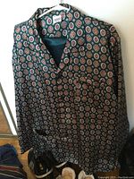 Silk pajama top, dark with multi-colored circular motifs, hanging.
