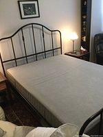 Black metal double bed frame with tall headboard featuring vertical bars and decorative elements, paired with light gray double mattress in bedroom setting.
