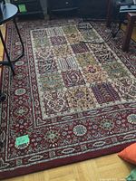 Full view of one Persian style rug showing patchwork pattern with red border, placed on hardwood floor surrounded by furniture.