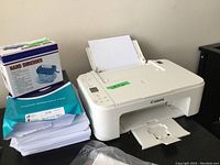 Canon Pixma printer loaded with paper, paper stack wrapped in blue packaging, and boxed manual hand shredder visible