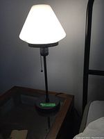 Two black metal bedside lamps with white matte glass shades on bedside tables, lit showing soft ambient light, each with pull chain switches.