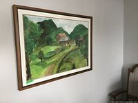 Side angled view of large framed watercolour painting on wall, showing countryside landscape with house and green hills.