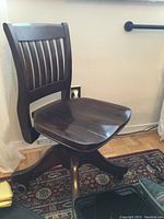 Small vintage wooden office chair with slatted back, dark wood finish and caster wheels
