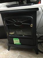 Front view of larger black vintage electric fireplace heater showing glass door with decorative metal design and brass handle