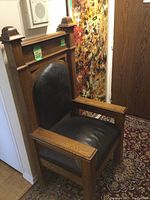 Three-quarter front view of one chair showing walnut frame, padded leather seat and tall back panel against patterned rug and abstract painting