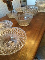 Eight clear cut crystal bowls arranged on wooden table, showing variety of patterns and sizes