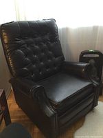 Front side view of vintage black vinyl recliner chair showing tufted backrest and rolled arm.