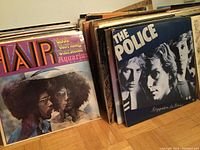 Front row of two stacks of vinyl records; visible covers include Good Morning Sunshine / Aquarius and Reggatta de Blanc by The Police