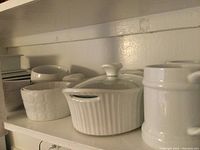 White ceramic bowls and casserole dish on shelf showing ribbed casserole with lid and bowls with embossed circular patterns.