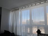 White sheer IKEA curtains hanging on a curtain rod over a large window. Curtains feature a square checked semi-transparent pattern and some panels are drawn to the side.