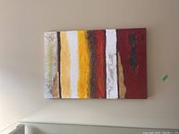 Photo of abstract mixed media painting on a wall showing full artwork with vertical textured stripes in various colors including white, yellow, red, brown, and black.