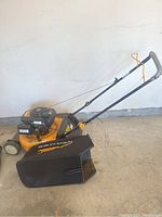 Full side view of the Club Cadet lawnmower showing handle, grass collection bag, and wheels on concrete floor.