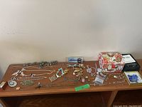 Wide view of tabletop displaying assorted costume jewelry including necklaces, brooches, earrings, watches, and decorative boxes