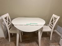 Front view of the white wooden dinette table partially extended with two chairs on each side.