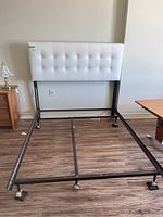 Full view of the metal bed frame with attached white faux leather button-tufted cushioned headboard, shown assembled on a wood floor.
