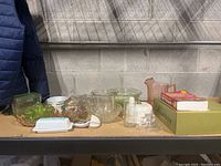 Overview of all glassware items on shelf including Pyrex butter dish, green juicer, pink pitcher, bowls, and other glass containers