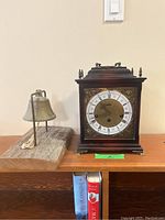 Photo of mantel clock and dinner bell on wooden table shelf