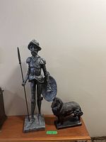 Photo of the Conquistador statue and metal dog placed on a wooden surface, showing full figures and relative size difference.