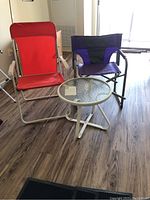 Two folding patio chairs and small round glass-top patio table placed indoors on wood flooring.