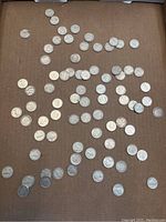 Top-down view showing spread of approximately 66 silver dimes on a brown surface, illustrating overall quantity and variety.