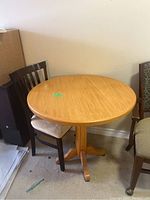 Round wooden pedestal table with dining chair behind it.