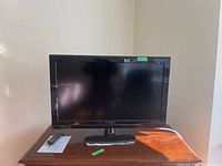 Front view of the 32 inch Dynex TV on stand, remote control placed beside it on a wooden surface.