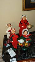 Front view of the full set displaying five Byers Choice Carolers dolls arranged on a black marble surface, showcasing their festive attire and stands.