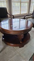 Round wood coffee table with ornate carved legs and open storage shelf below