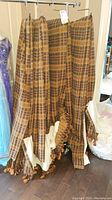 Four brown/beige plaid patterned drapery panels hanging on a metal rack, showing full length and pleating details.