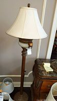Full view of the floor lamp with bell-shaped cream fabric shade and ornate wooden base.