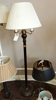 Full view of the metal floor lamp with white pleated lampshade, showing the lamp standing next to other lampshades and lamps.