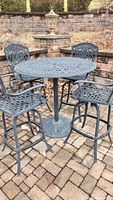 Full view of round patio table with four matching armchairs arranged on stone paver patio with retaining wall backdrop