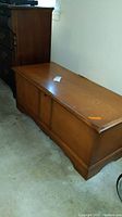 Photo of the front and top of a rectangular wooden cedar chest with a lock, showing scratches and wear.