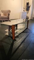 Full side angle view of the media stand showing glass top, metal frame, wooden legs, and two glass shelves below.