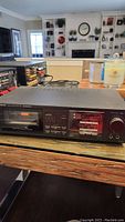 Front view of Onkyo cassette player showing cassette compartment, control buttons and knobs on wooden table.