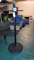 Full view of the black metal pool towel rack standing on basement floor with three arms for hanging towels.