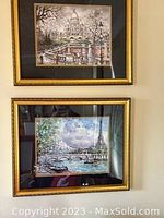 Photo showing two framed Paris prints hung on a wall. The top print features the Sacré-Cœur Basilica, and the bottom print features the Eiffel Tower with boats on the river. Both framed in gold frames with black matting.