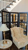 Divider displayed from front view next to beige armchair and lamp, showing all three panels