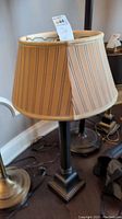 Full view of metal table lamp with striped fabric shade on dark wood floor beside other lamps.