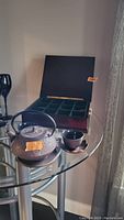 Overall tea set displayed on glass table, showing teapot, two cups with saucers, and open wooden tea box with compartments.