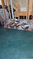 Full view of large rectangular metal floral art piece leaning against a wooden frame structure on floor.