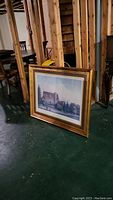 Framed large print of European cathedral resting against wood construction framing in basement, showing full frame and part of image.