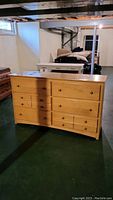Full front view of light wood dresser with six drawers in basement setting showing overall condition and surroundings.