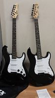 Photo of two black electric guitars standing upright, showing full body and neck including headstocks and strings.