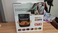 Photo of one TROTTRONICS Essential Air Fryer box showing front packaging with image of fryer, food, and people cooking as well as the 50 recipe cookbook indication.