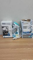 Two handheld garment steamer boxes and one steamer out of box wrapped in plastic on wooden surface.